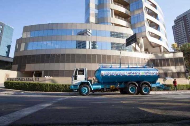 Caminhão-pipa azul e branco em operação abastecendo reservatório de água em área industrial, mangueira conectada, fim de tarde, fotografia realista, paleta azul e cinza